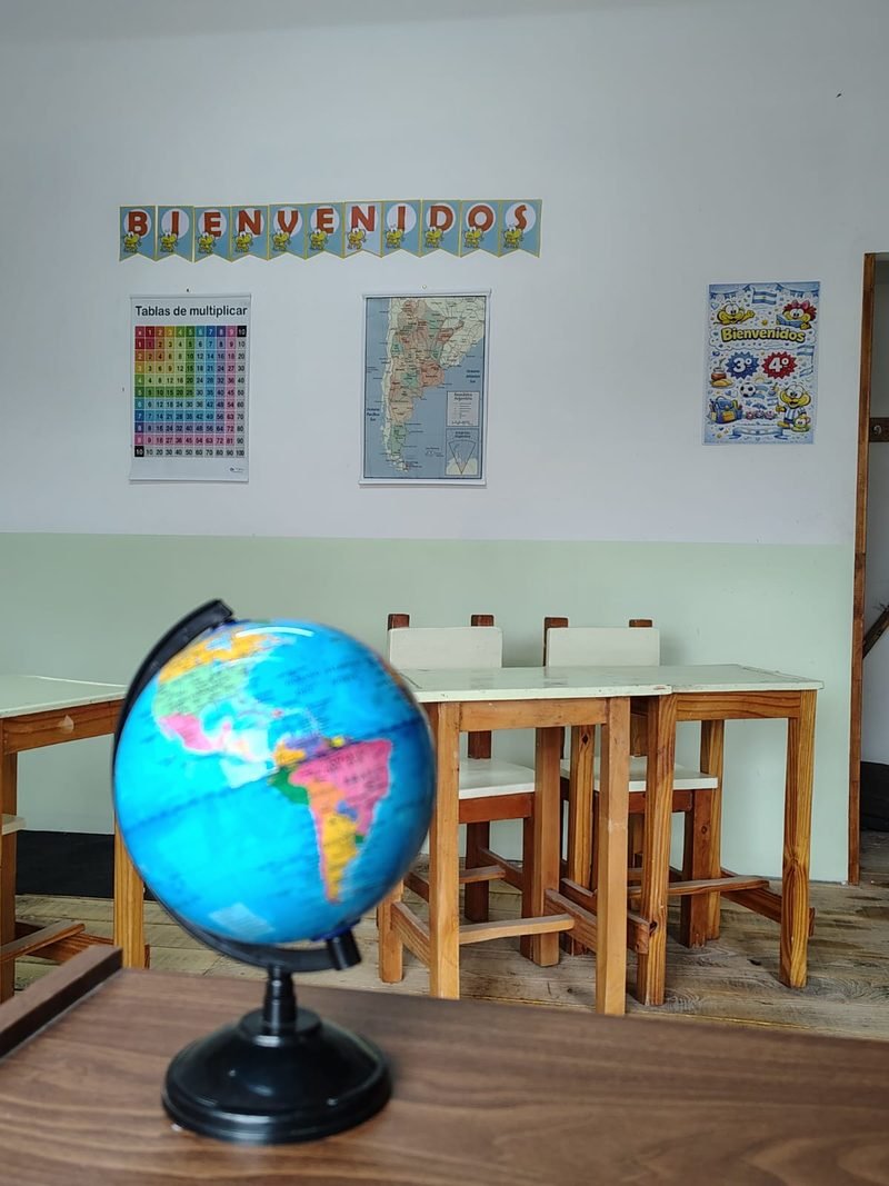 Globo terráqueo sobre un escritorio en un aula con tablas de multiplicar, mapa y guirnalda de bienvenida