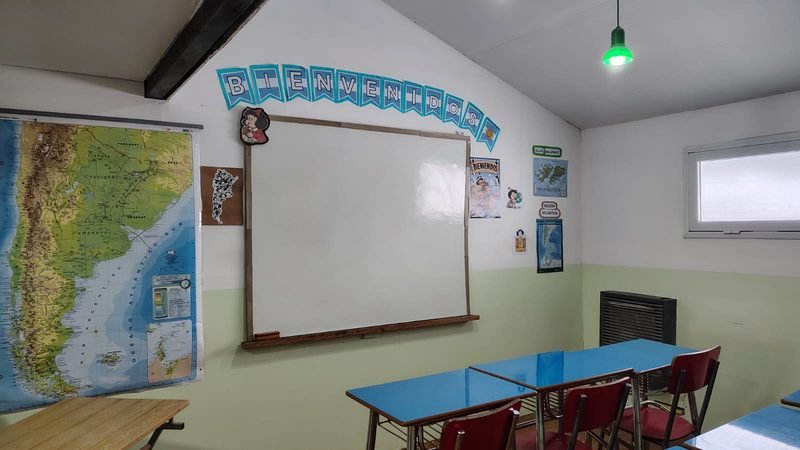 Aula de primaria con mapa de Argentina, pizarra blanca, guirnalda de bienvenida y mesas celestes