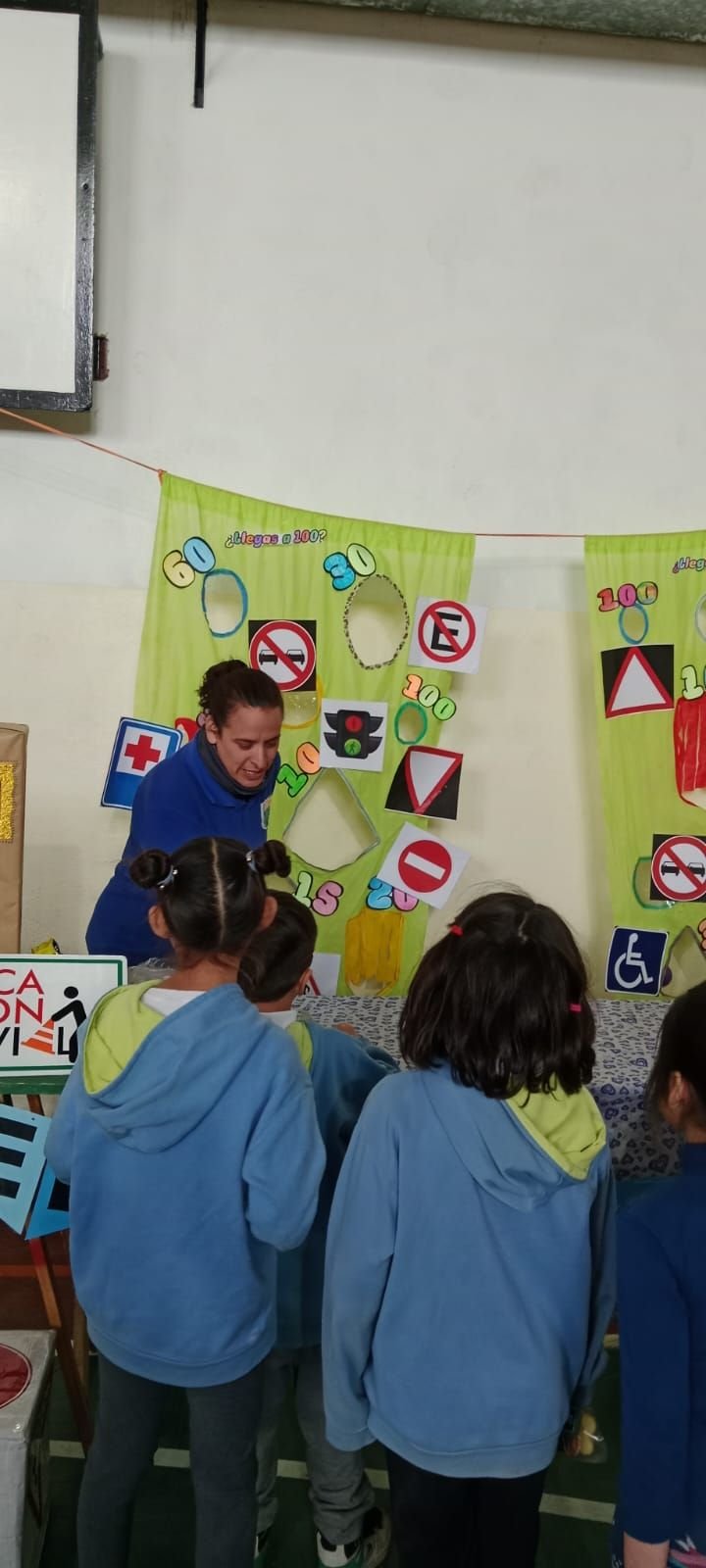 Taller de Educación Vial: alumnas y alumnos de espaldas frente a una docente y un panel con señales de tránsito y velocidades máximas
