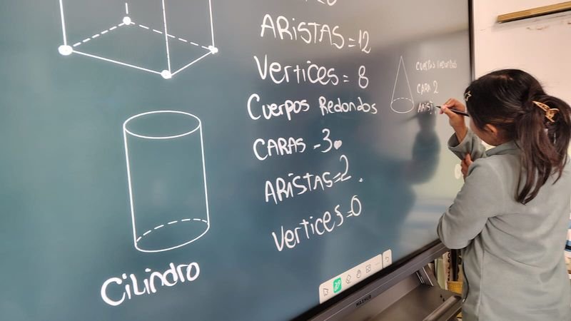 Alumna de Cielos Abiertos escribe cuerpos geométricos en una pantalla inteligente del aula